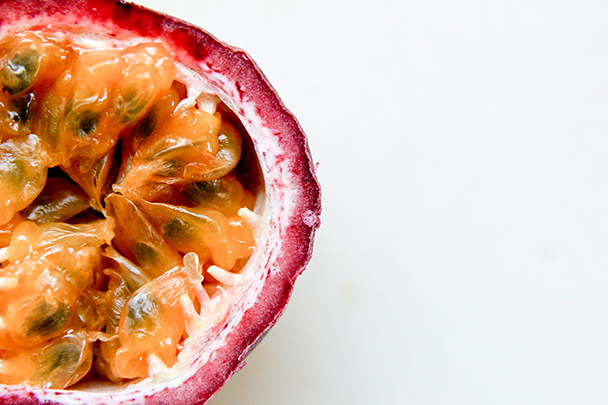 Nahaufnahme einer aufgeschnittenen Passionsfrucht mit orangefarbenem Fruchtfleisch und schwarzen Kernen vor hellem Hintergrund