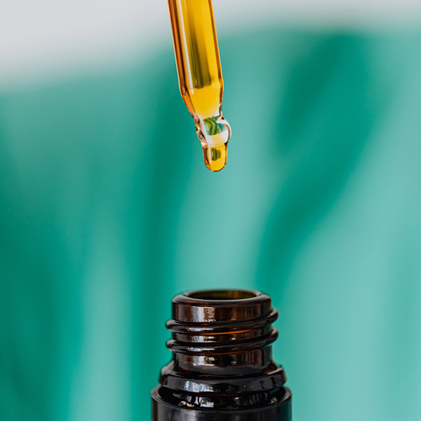 Bernsteinfarbener Tropfen Öl aus einer Pipette über einer dunklen Glasflasche – Symbolbild für antioxidativen Hautschutz mit Vitamin E