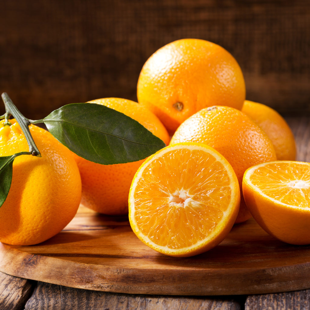 Frische Orangen mit grünen Blättern, teils aufgeschnitten, auf Holzbrett – Quelle für Citrus Aurantium Dulcis (Orange) Peel Oil.