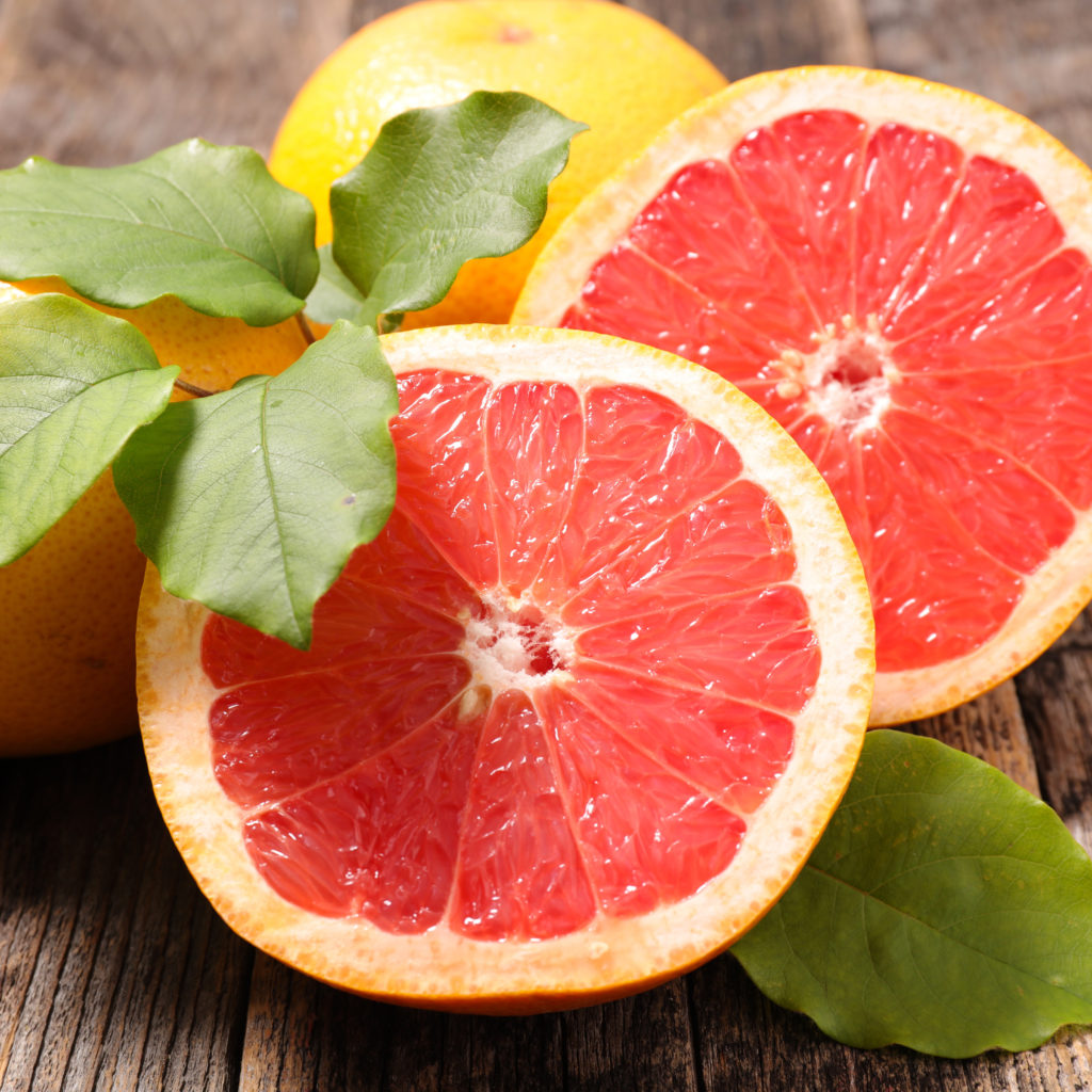Aufgeschnittene rosa Grapefruit mit grünen Blättern auf Holzuntergrund – Quelle von Citrus Grandis (Grapefruit) Peel Oil.