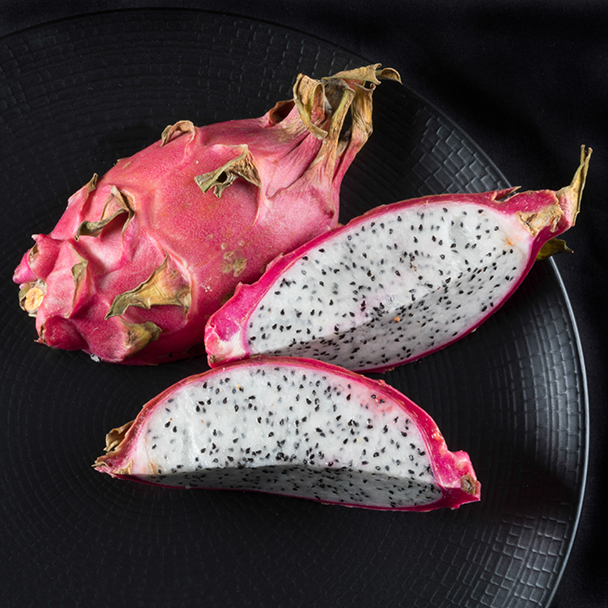 Aufgeschnittene Drachenfrucht mit weißem Fruchtfleisch und schwarzen Samen auf einem schwarzen Teller