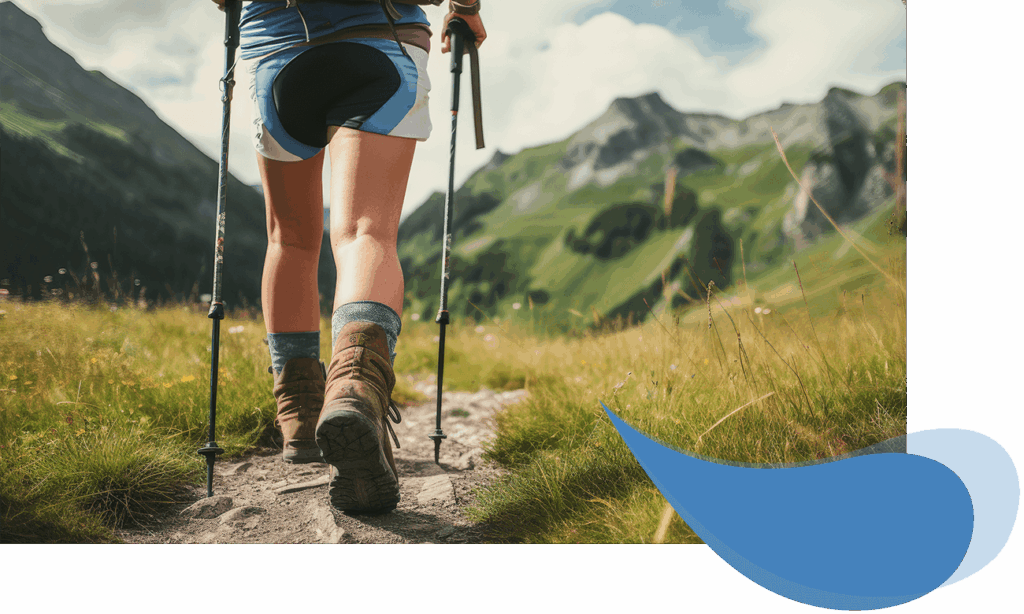 Person beim Wandern auf einem Gebirgspfad, Fokus auf Beine und Wanderstiefel, Berglandschaft im Hintergrund.