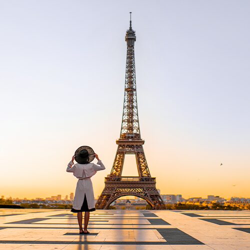 Frau mit Hut blickt auf den Eiffelturm bei Sonnenaufgang – Symbol für Fernweh, Reisen und exklusive Gewinnspiele.