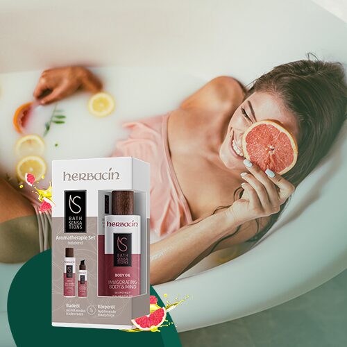 Frau entspannt in einer Badewanne mit Milchbad und Zitrusfrüchten, hält eine halbe Grapefruit vor ihr Gesicht; im Vordergrund das Herbacin Bath Sensations Aromatherapie-Set mit Badeöl und Körperöl – für ein belebendes Pflegeerlebnis.