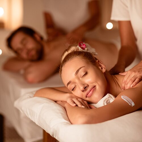 Frau und Mann genießen gleichzeitig eine Massage in entspannter Spa-Atmosphäre mit Kerzenschein – Symbol für ein romantisches Wellness-Wochenende zu zweit.
